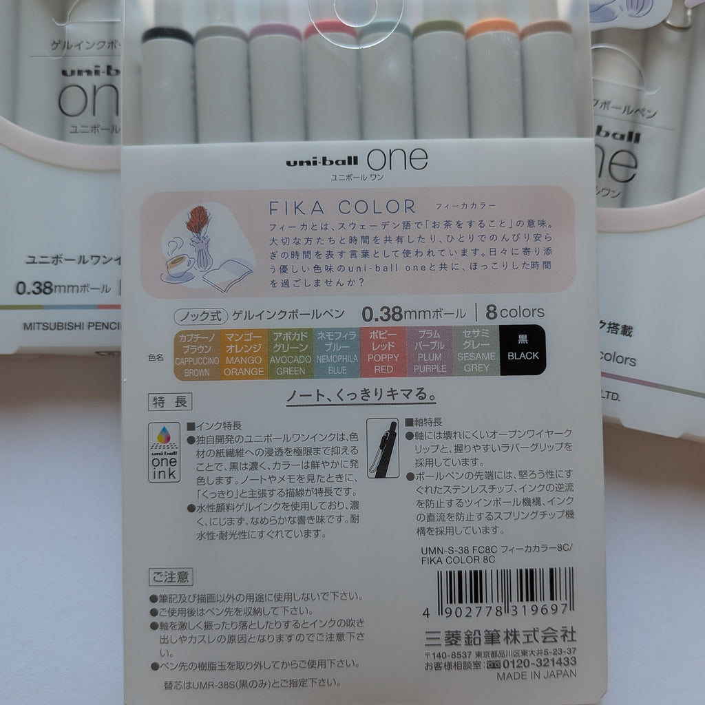 A package of Uni-ball One Fika Color gel pens shown from the back, displaying the white cardboard backing with Japanese text, a color chart, and a barcode. The pens inside have black barrels with colored tips visible at the top.