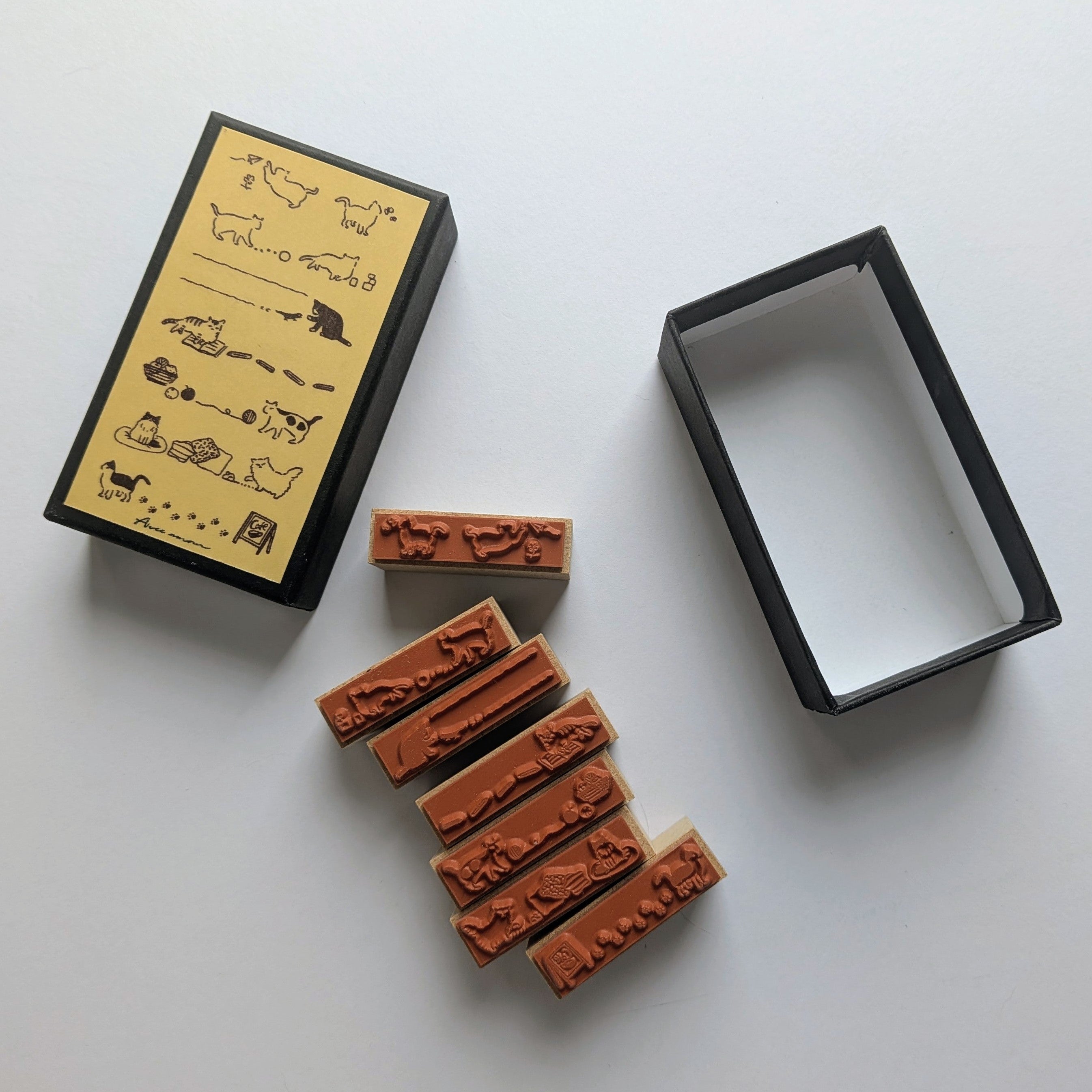 A set of rubber stamps with cat-themed engravings, shown alongside their black and yellow storage box on a light gray background.