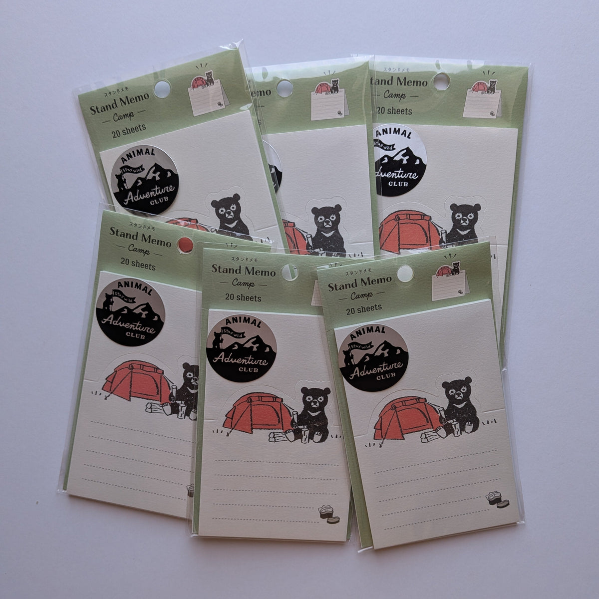 Six small packaged memo cards arranged on a plain light background. Each card package has a pale green border, a black-and-white mountain-and-bear logo.