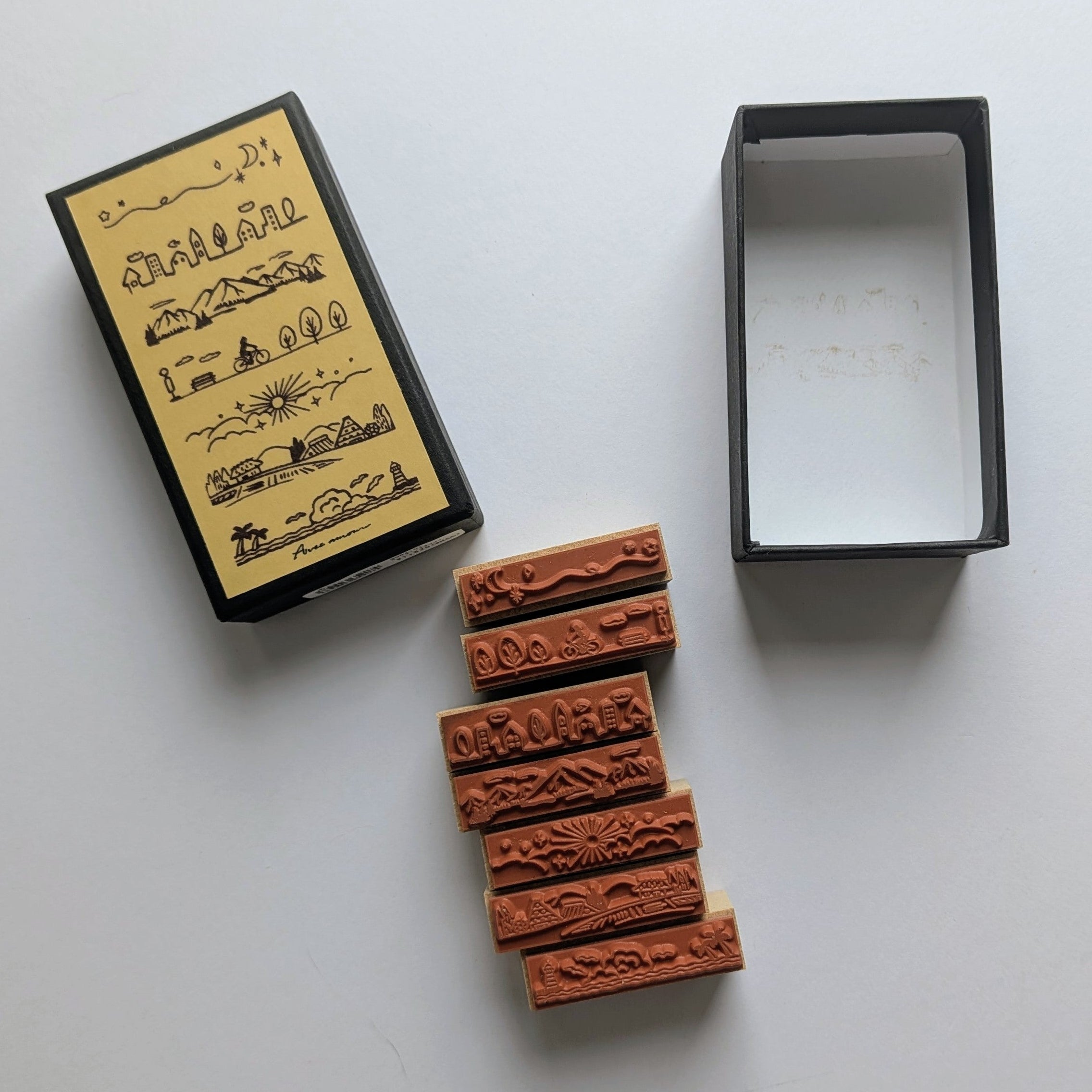 A set of rubber stamps with carved scenery illustrations, shown alongside their black and yellow packaging box on a clean white background.
