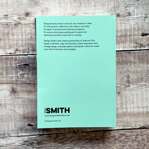 A mint green notebook page with printed text, photographed flat on a rustic weathered wood background. The page features the title 'Design Smith' and website 'www.