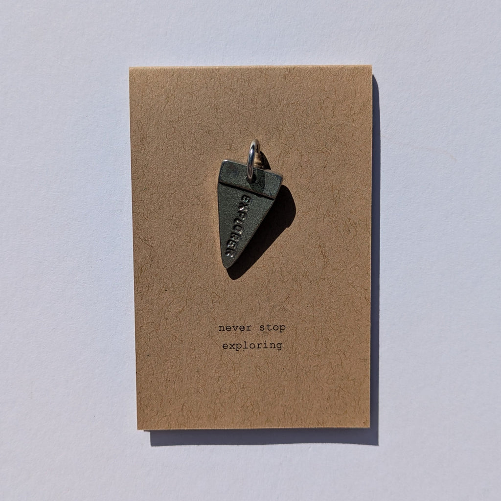 Journal metal charm on a brown card with 'never stop exploring' text on a white background
