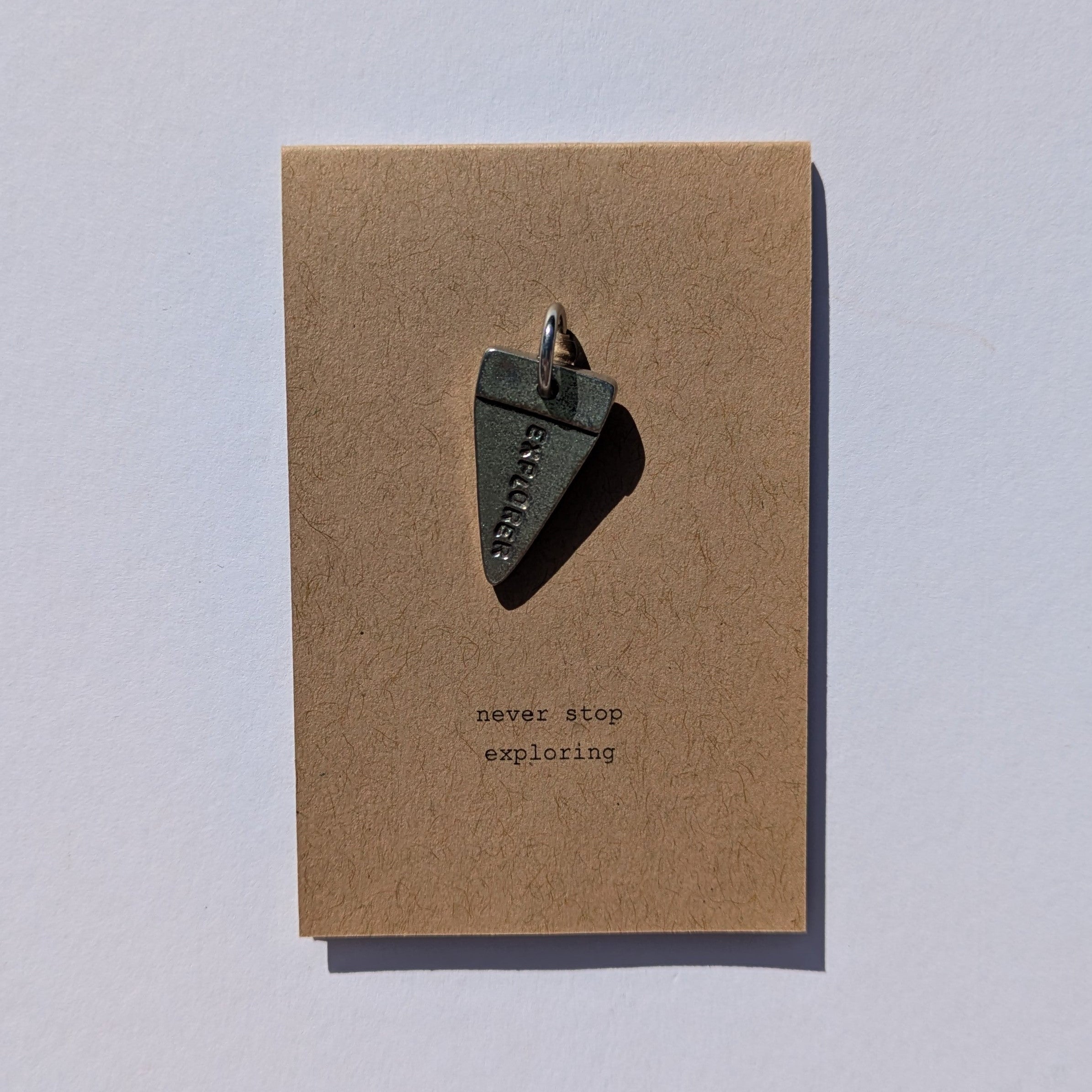 Journal metal charm on a brown card with 'never stop exploring' text on a white background