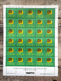 A sheet of postage stamps laid flat on a rustic wooden surface. Each stamp has a green background with a yellow crescent and brown snail illustration, plus the text 'A little love, by small mail.