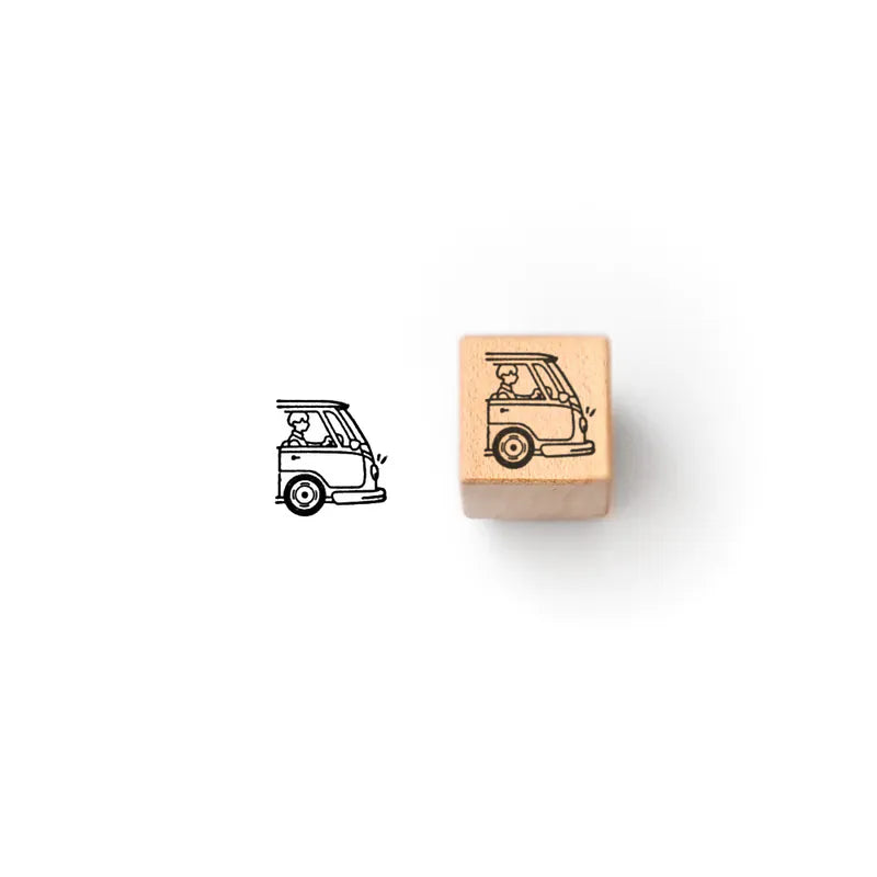 A wooden rubber stamp block with a camper van illustration on a light wood cube, shown next to the stamped black ink design on a plain white background.