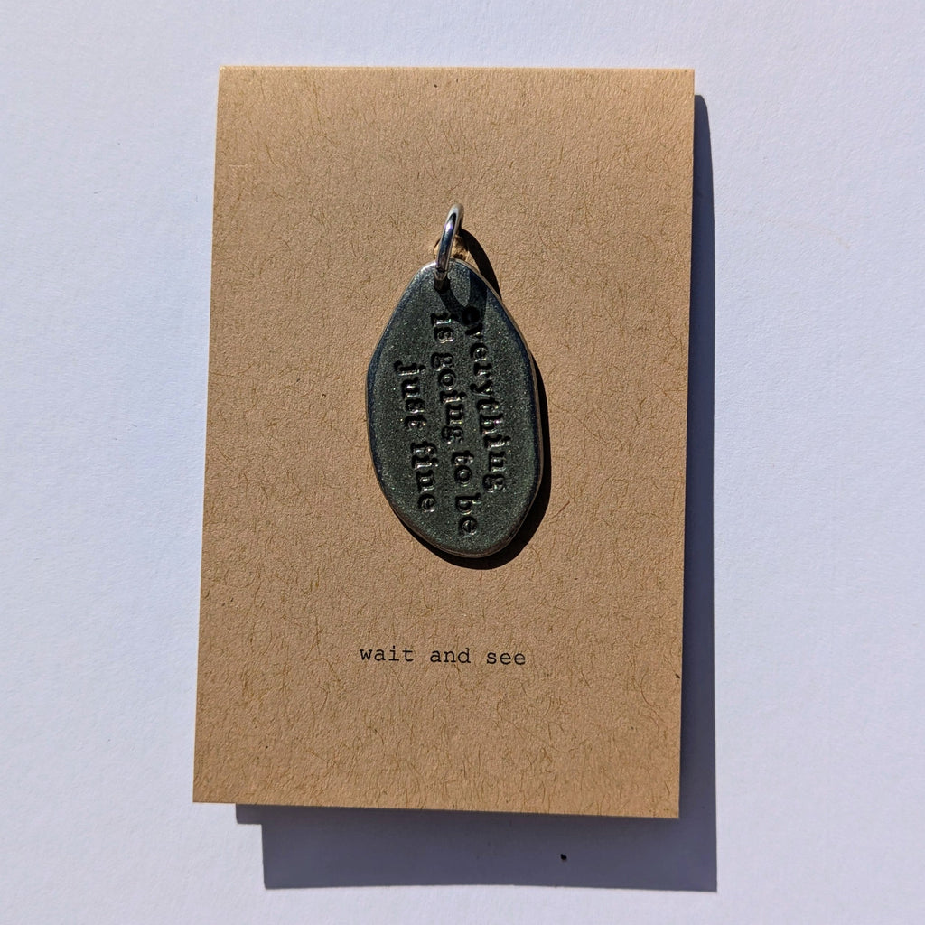 Metal charm with everything is going to be just fine printed on a brown card with text on a light gray background