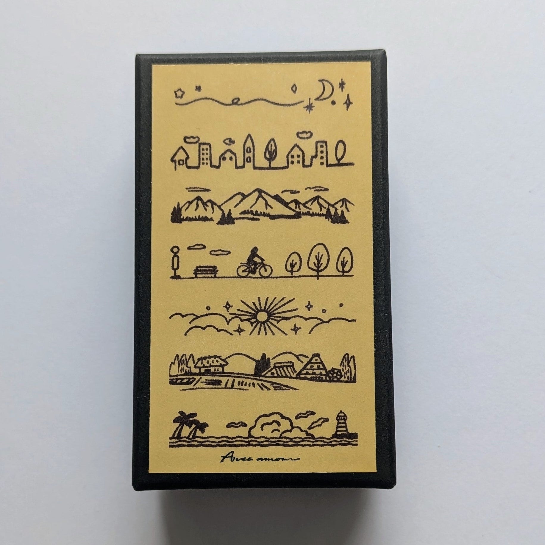 A rectangular black box with a cream-colored front panel featuring black hand-drawn landscape illustrations and the text 'Avec Amour' at the bottom, photographed on a light gray background.