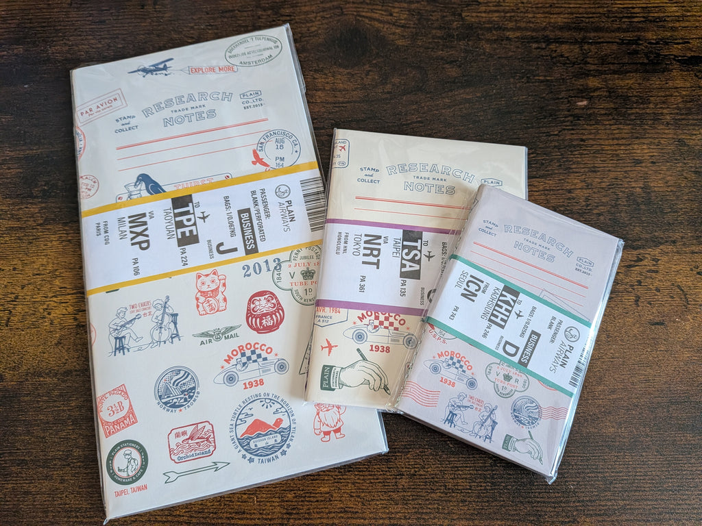 Three small passport-style envelope notebooks with colorful travel stamps and postmarks, arranged on a dark wooden tabletop.