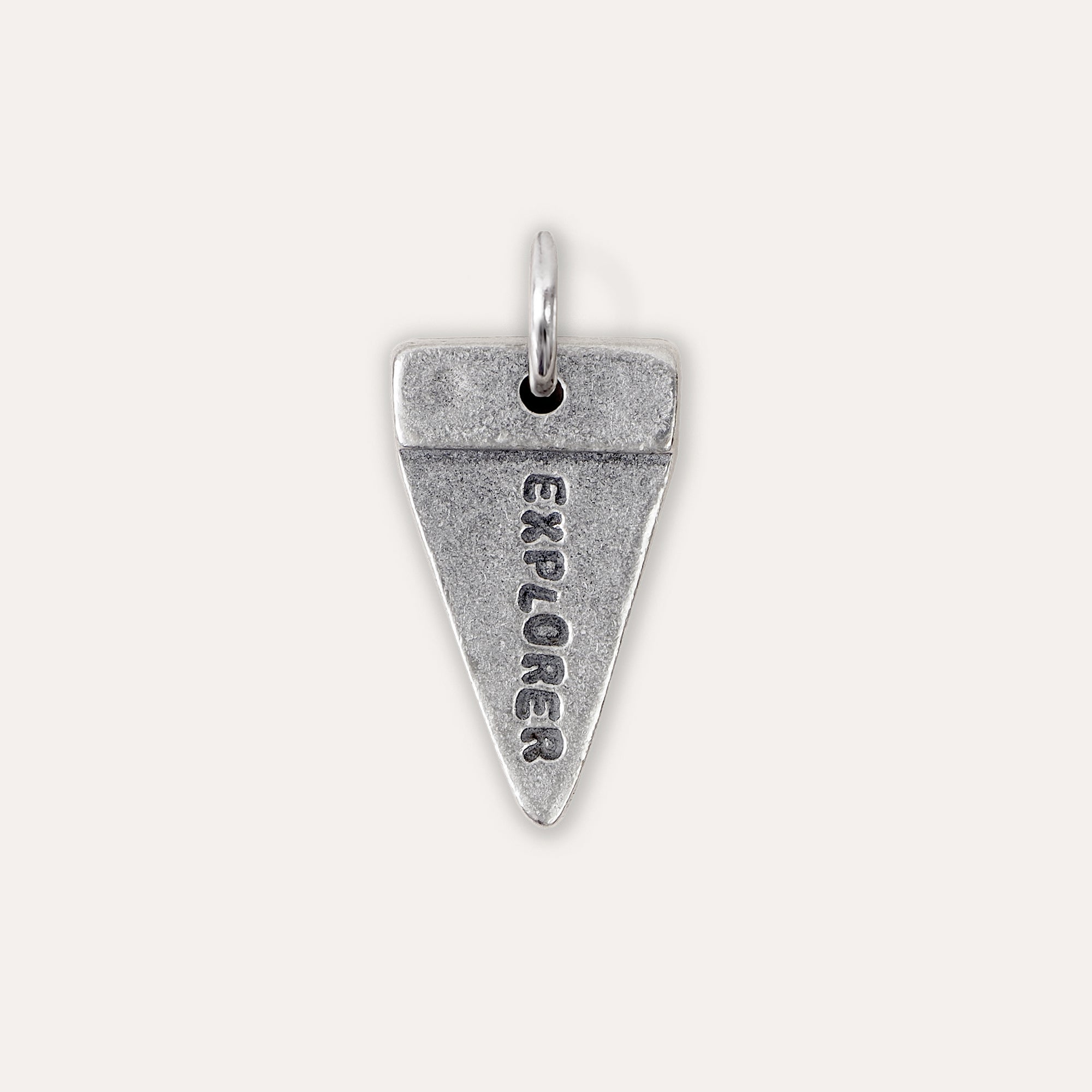 A silver triangular pendant charm engraved with the word 'EXPLORER' vertically, shown on a light beige background.