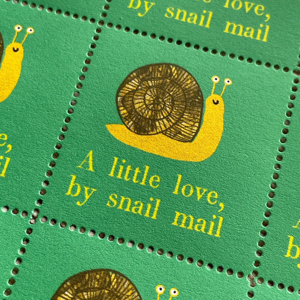 A close-up of a green postage stamp sheet featuring yellow snail illustrations and the phrase 'A little love, by snail mail' printed in yellow text.