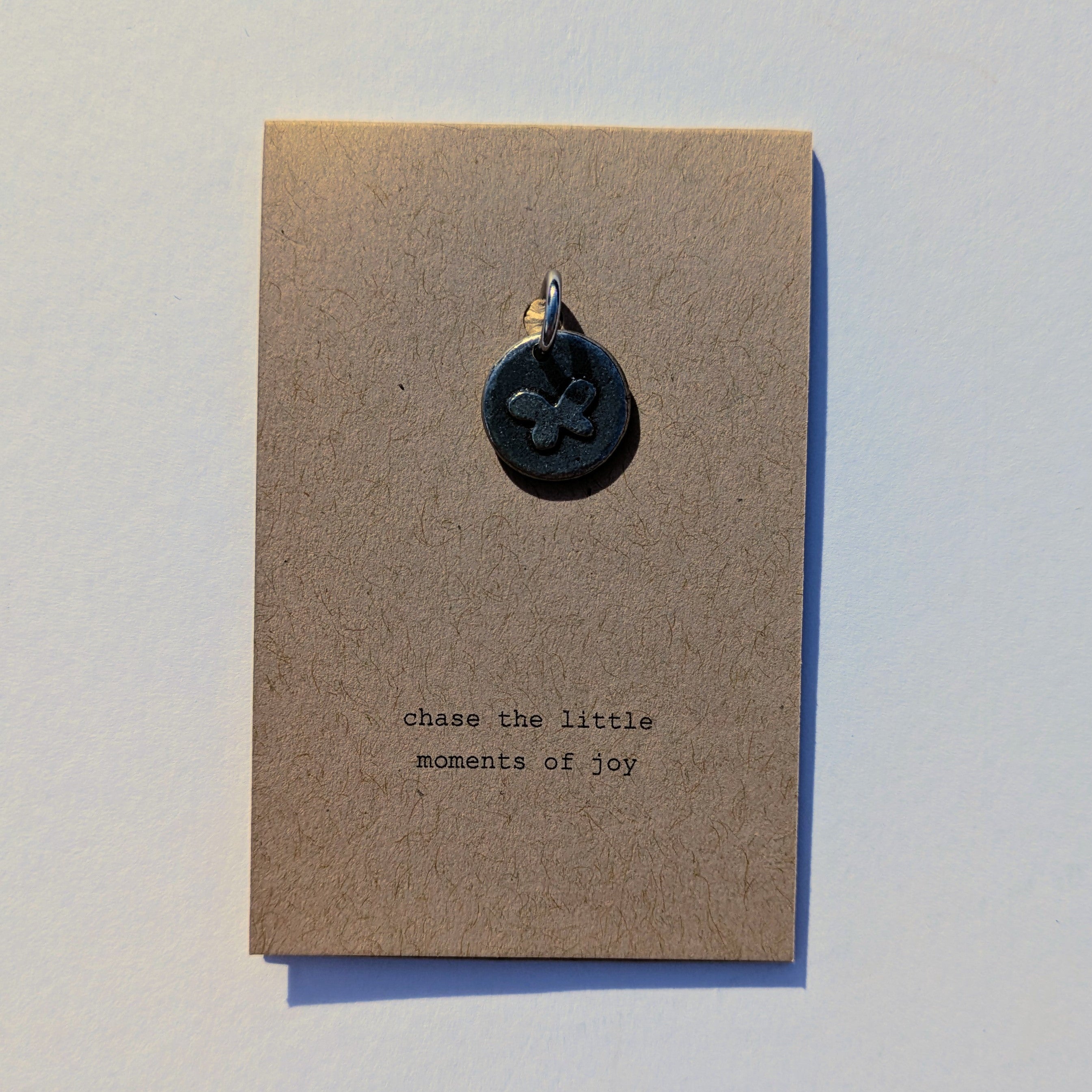 Metal pendant on a brown card with 'chase the little moments of joy' text