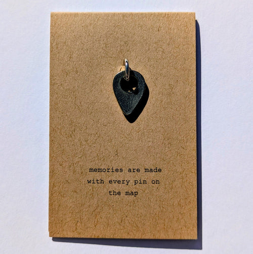 Metal map pin on a brown card with text 'memories are made with every pin on the map' on a light gray background
