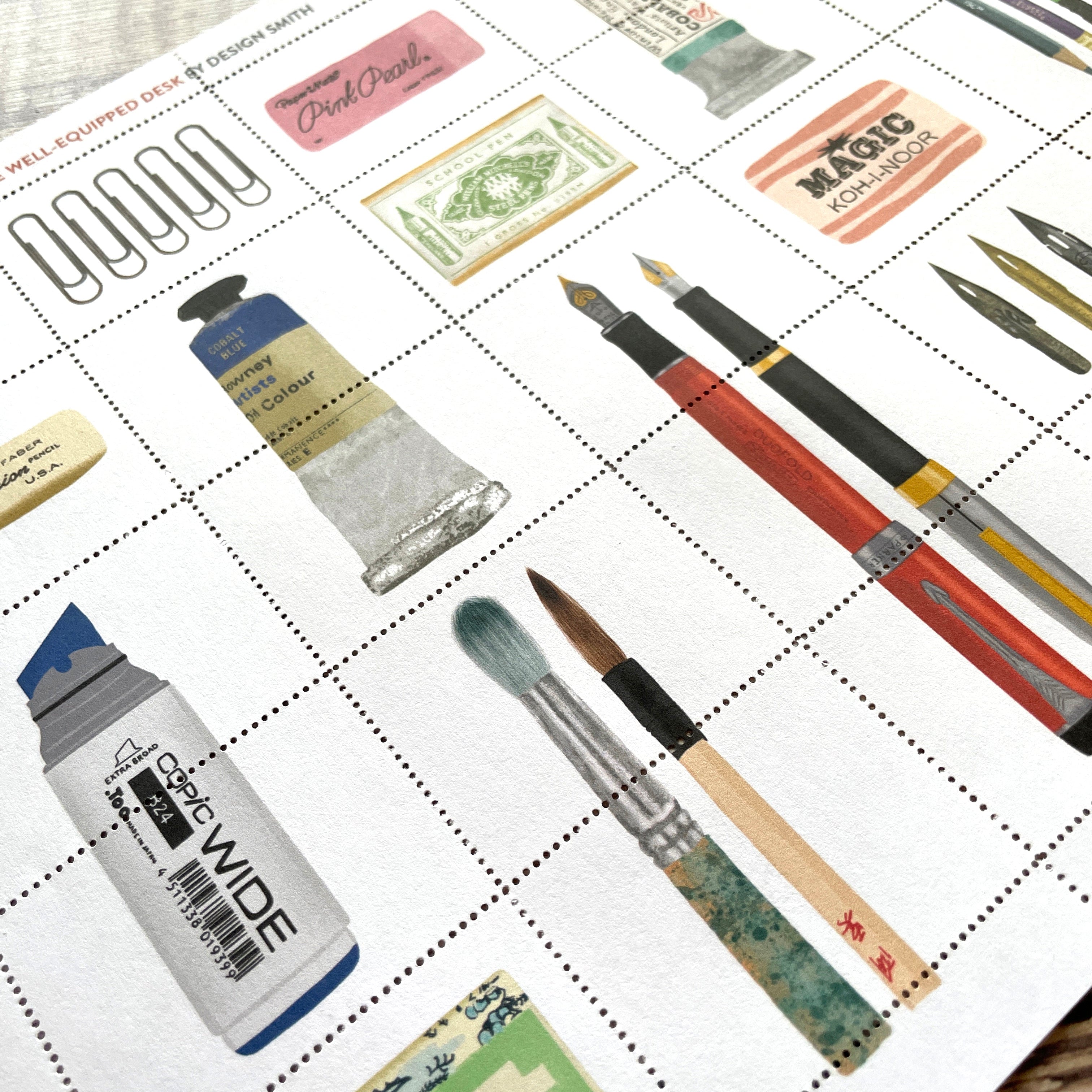 A printed sheet of stamp paper featuring illustrated art supplies arranged in a grid, including paint tubes, brushes, pencils, and ink pens. The sheet is photographed at an angle on a wooden surface.