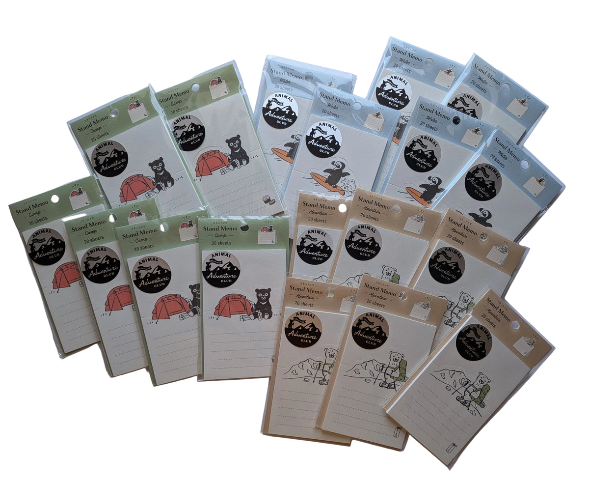 A collection of small camping-themed notepad sheets arranged on a light gray background. The notepads feature illustrated scenes including a bear with a tent, a campfire, and a mountain landscape, with different color accents in green, orange, red, blue, and beige.
