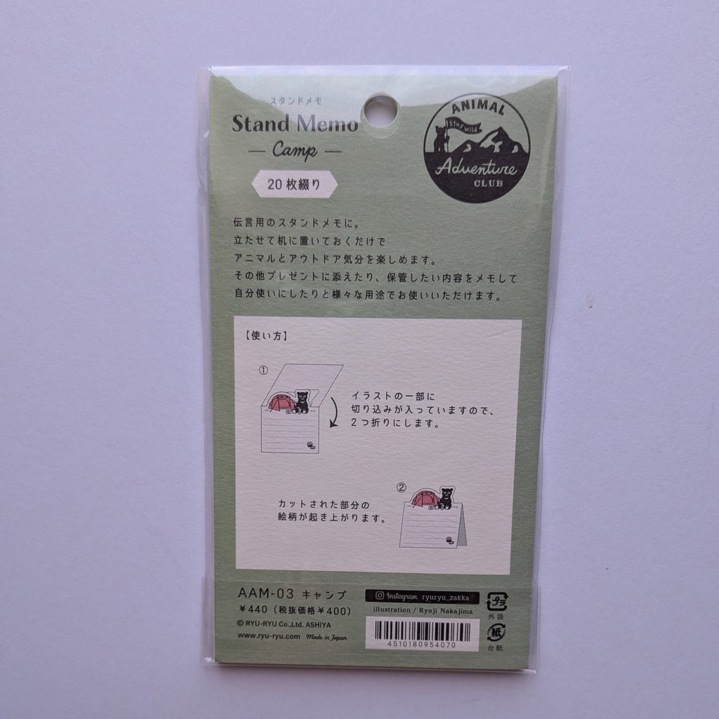 A packaged Japanese 'Stand Memo Camp' memo pad set by Animal Adventure, shown in its original light green carded packaging against a light lavender background.