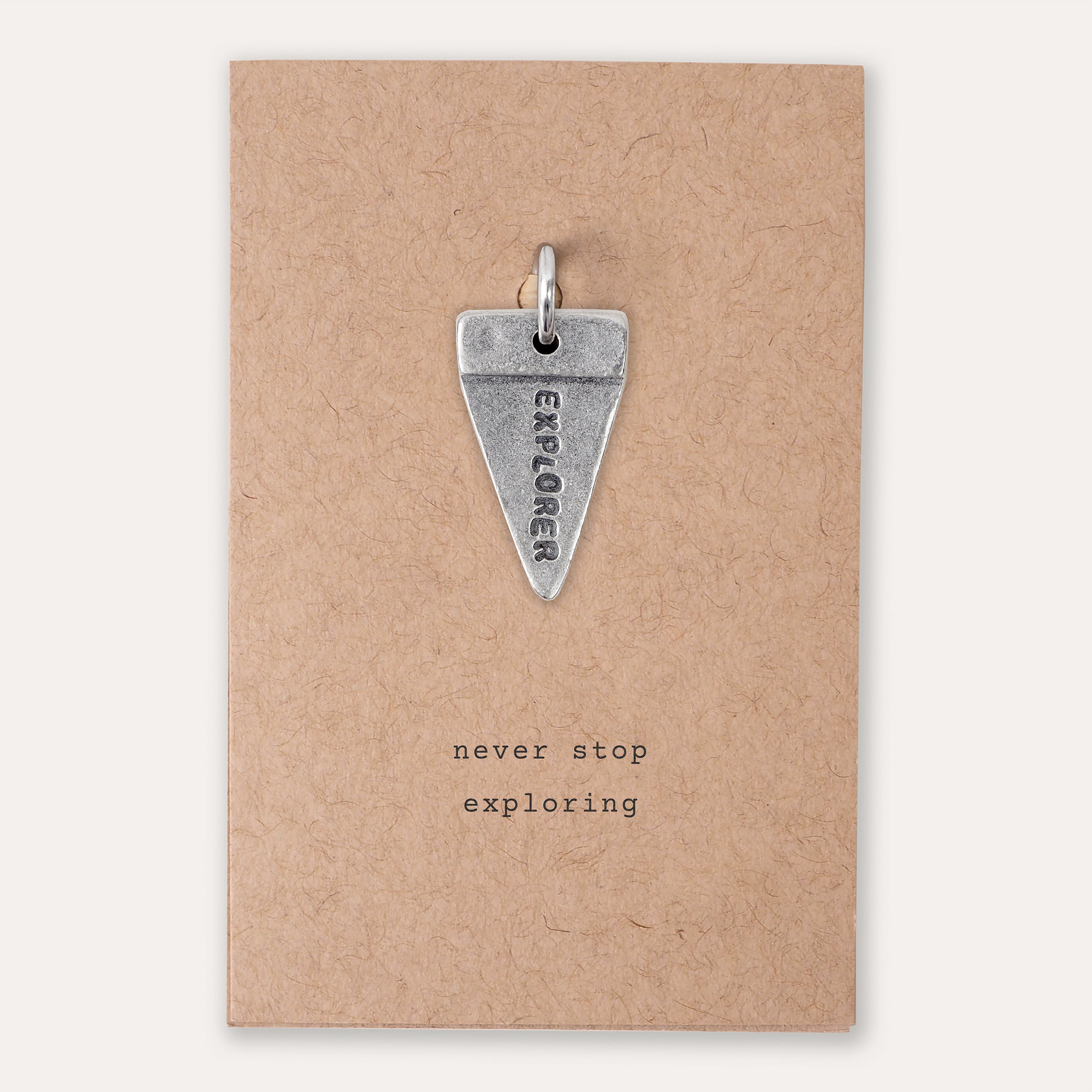 A silver triangular pendant engraved with the word 'EXPLORER' and a small loop at the top, displayed on a kraft paper backing card with the printed phrase 'never stop exploring'.