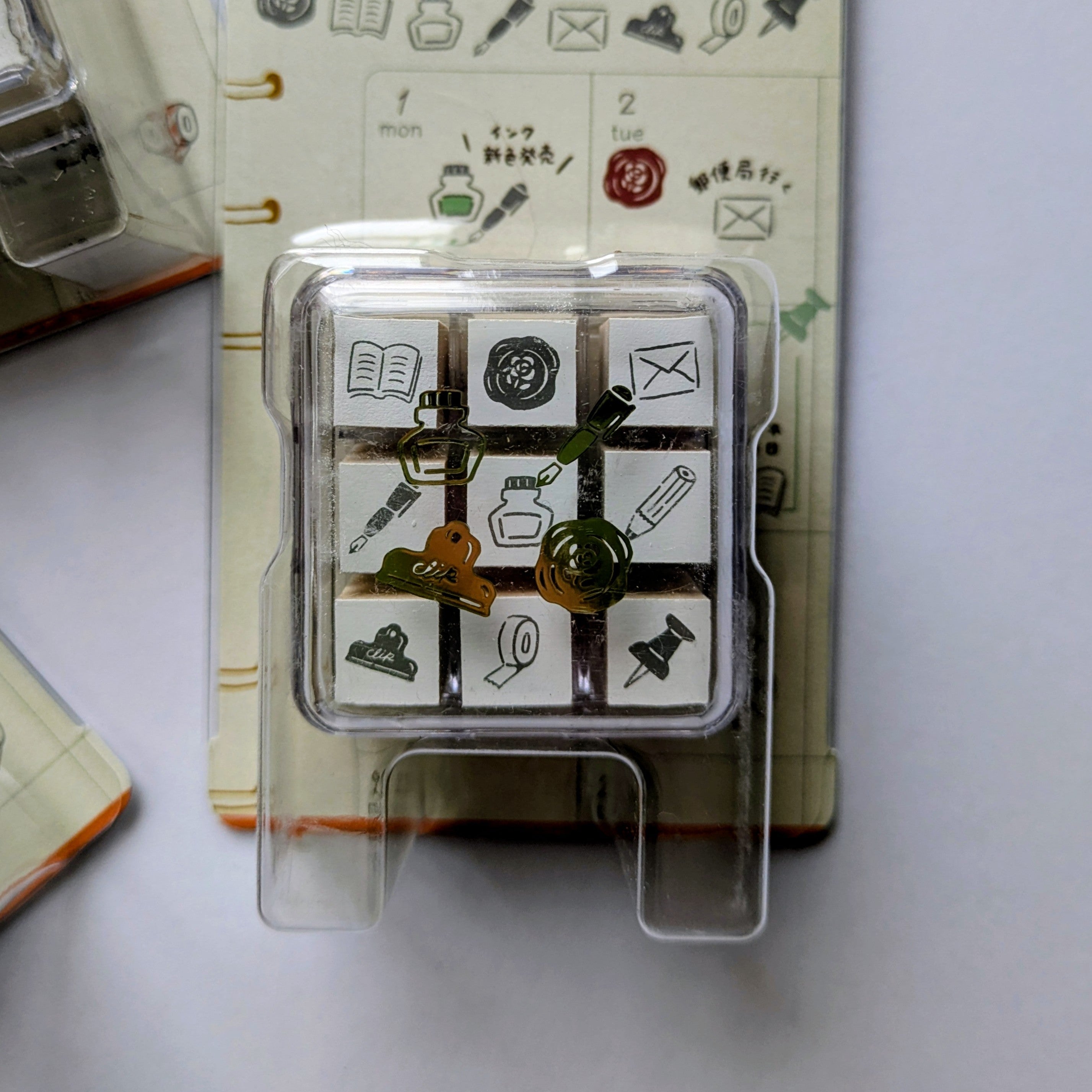 Set of decorative stamps with stationery illustrations on a clear plastic card, placed on a notebook.