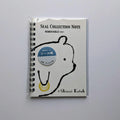 A spiral-bound notebook sealed in a clear plastic sleeve, featuring a white cover with a black bear outline, the text 'SEAL COLLECTION NOTE' and 'REMOVABLE', a blue circular sticker, and '© Shinzi Katoh' at the bottom, photographed on a light gray background.