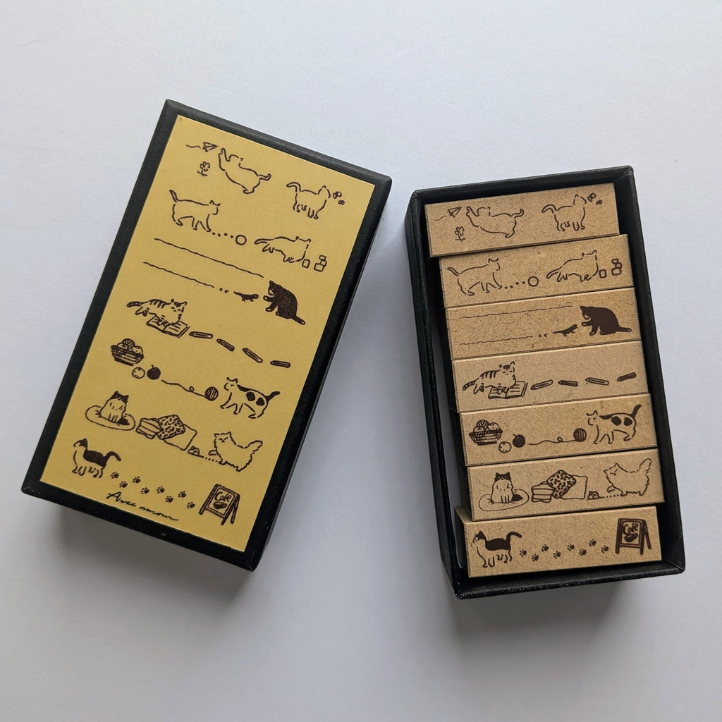 Sanby Cat-themed rubber stamps shown open, alongside their matching black and yellow storage box. The stamps feature various cat illustrations and the brand name Avec Amour is visible in the bottom-left corner of the box cover.