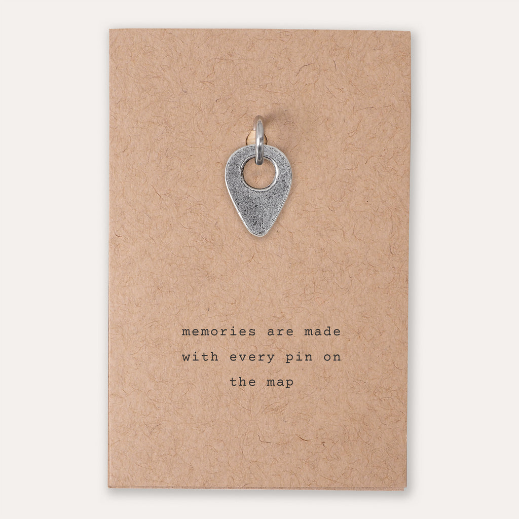 A silver drop pin location pendant charm displayed on a brown kraft paper backing card with the printed quote 'memories are made with every pin on the map'.