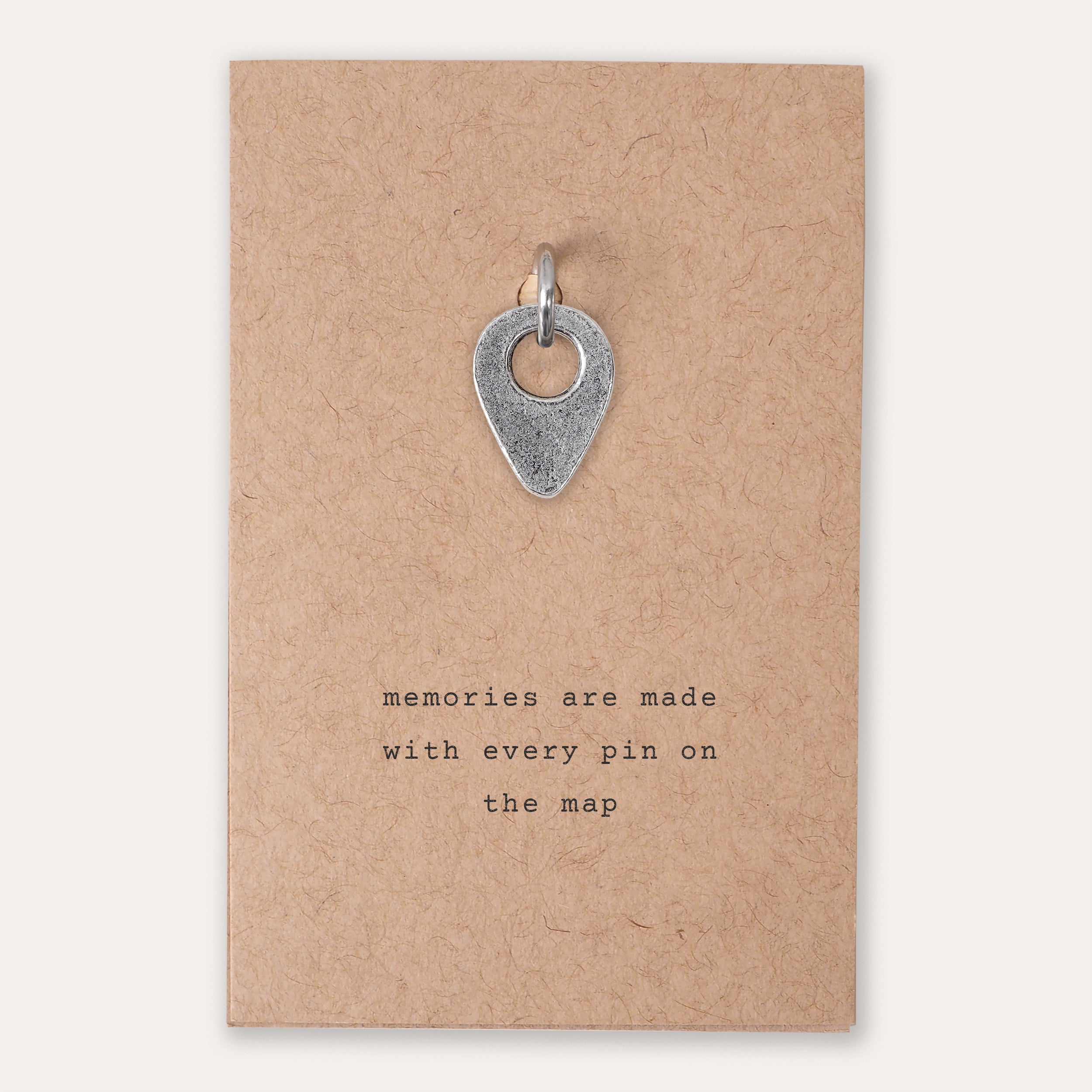 A silver drop pin location pendant charm displayed on a brown kraft paper backing card with the printed quote 'memories are made with every pin on the map'.