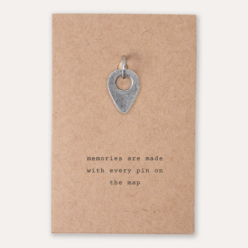 A silver drop pin location pendant charm displayed on a brown kraft paper backing card with the printed quote 'memories are made with every pin on the map'.