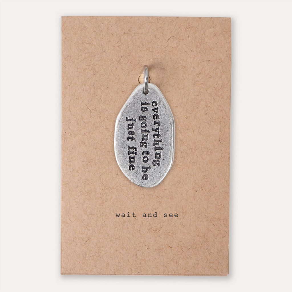 A silver-toned metal pendant with the phrase 'everything is going to be just fine' in black lettering, displayed on a brown kraft paper backing card that reads 'wait and see'.