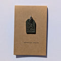 Metal plane tag shaped pendant on a brown card with 'adventure awaits' text